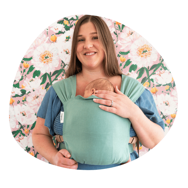 A white plus sized woman smiles at the camera while wearing her newborn in a hope&plum Sprout Newborn Carrier on her front
