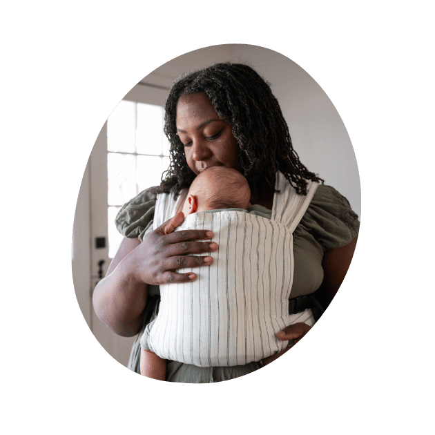 A BIPOC plus size woman looks down and embraces her infant worn on her front in a hope&plum Sprout Newborn Carrier