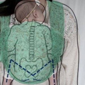 A baby is worn on their caregiver's front in a hope&plum Cove baby wrap. A green highlight showing the support provided and a blue dotted-line M are overlaid on baby's body.