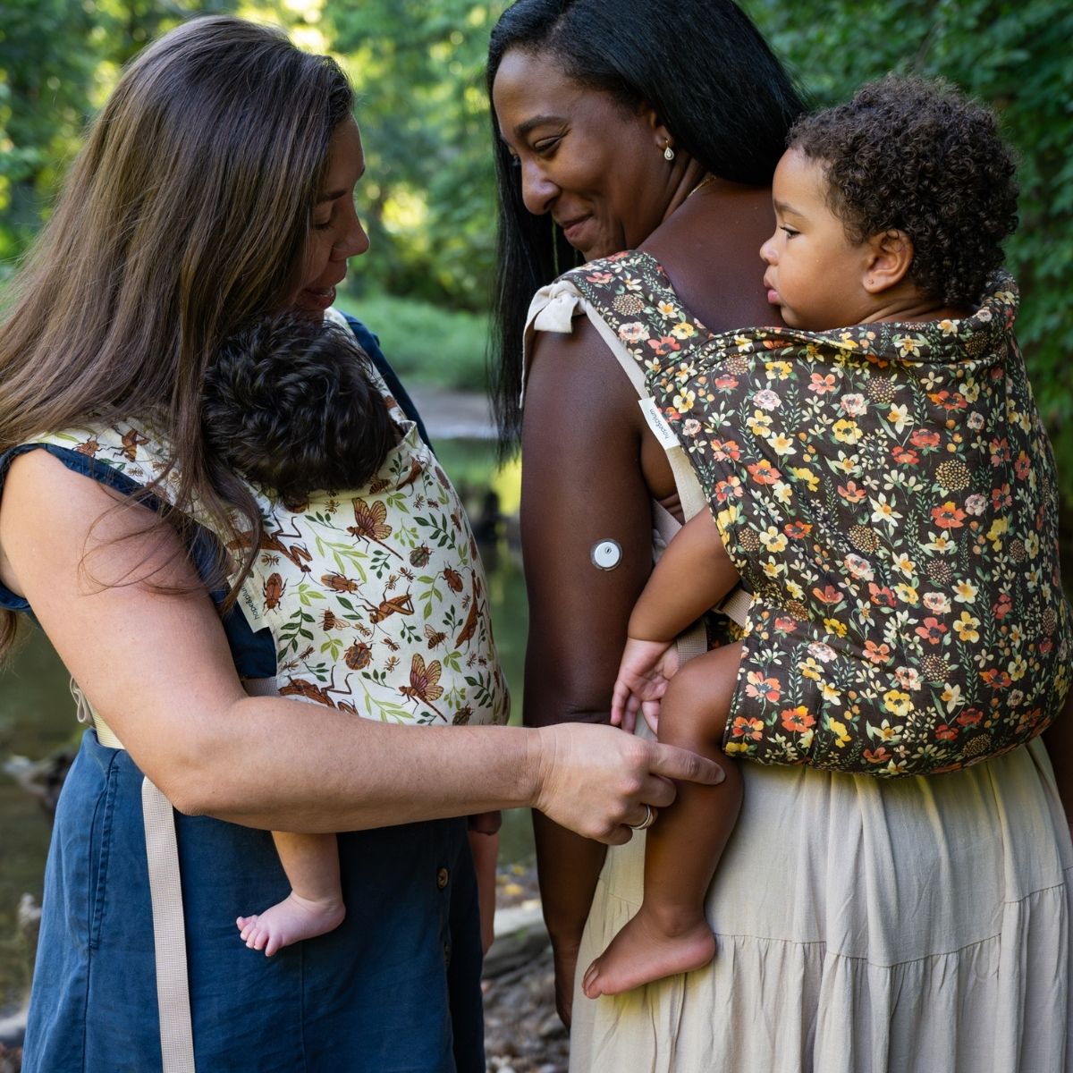 Two women stand in a forest while wearing their babies in hope&plum buckle carriers
