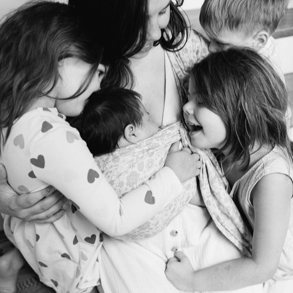A black and white photo of a mom in a group hug with her 3 children as she wears her 4th newborn on her front in a ring sling
