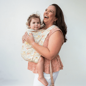 A woman wears her baby in a kid Lark on her front. She looks upward and laughs while baby looks at the camera.