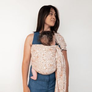 A straight size BIPOC woman wears a baby on her front in a hope&plum Woodland ring sling
