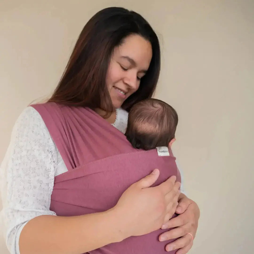 A straight size BIPOC woman looks down at and embraces her baby worn in a stretchy wrap on her front