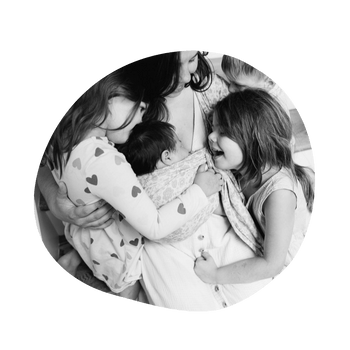 A black and white photo of a mom in a group hug with her 3 children as she wears her 4th newborn on her front in a ring sling