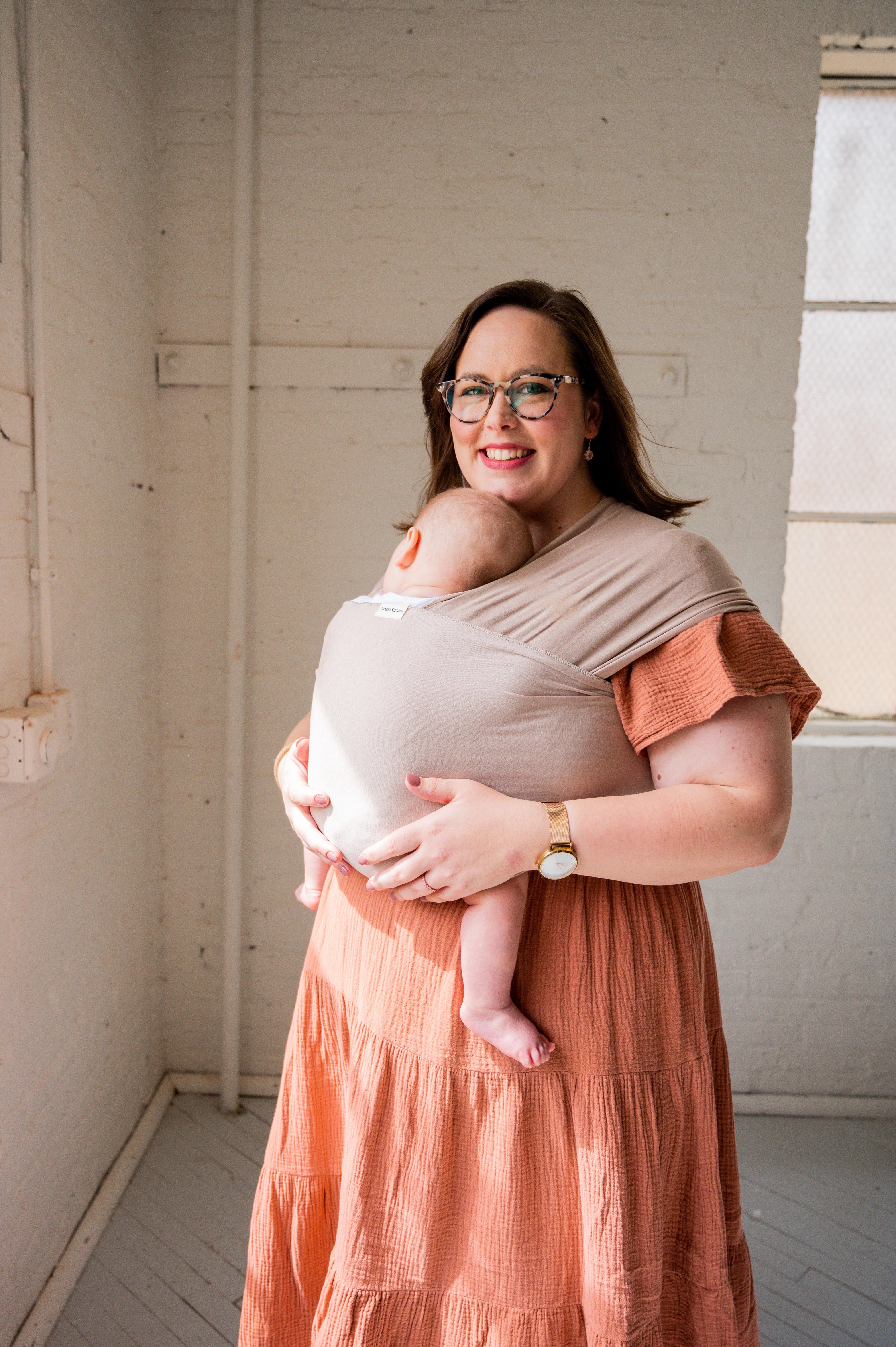 Plus-size mother wearing baby in tan-colored baby wrap.