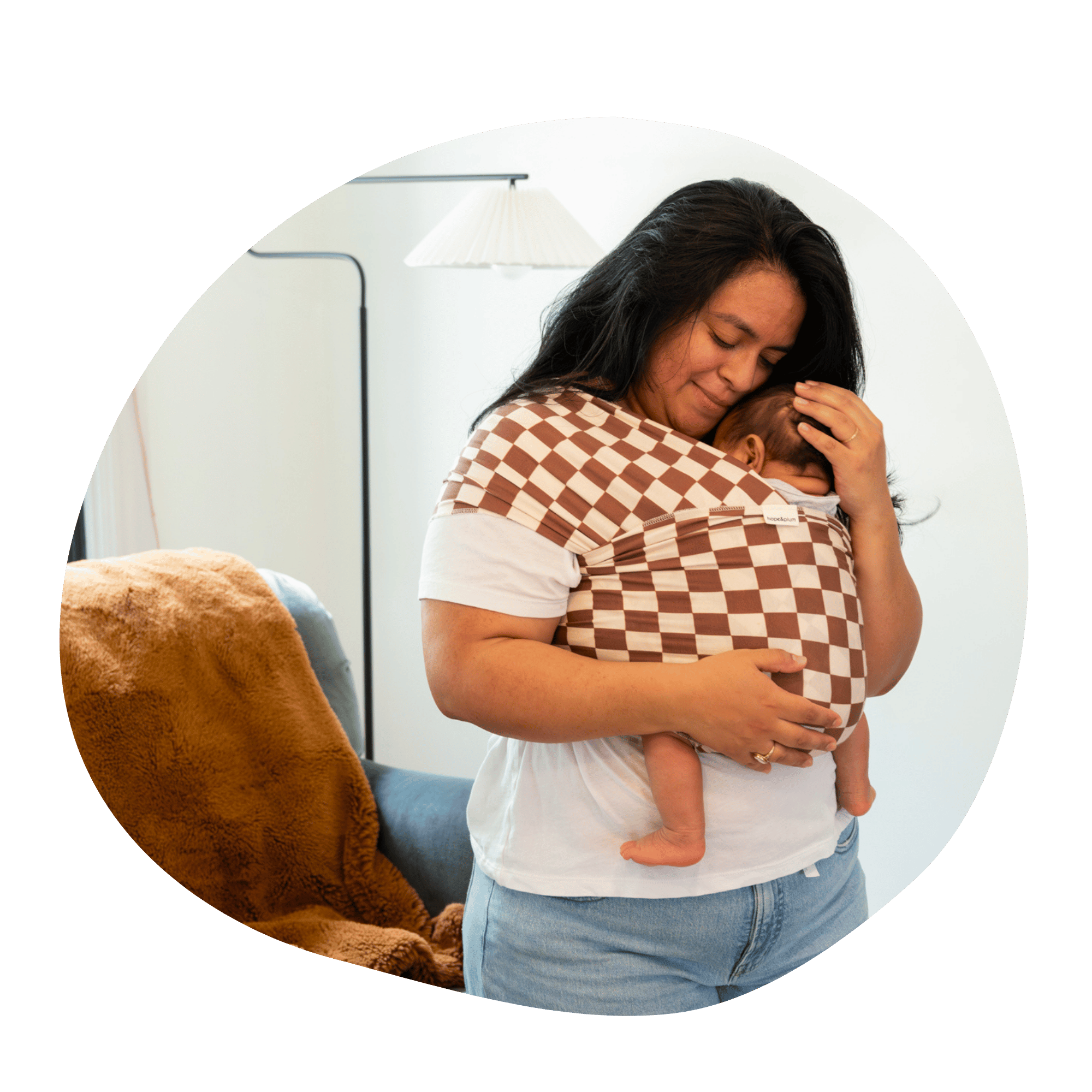 woman with black hair smiling and snuggling her newborn baby in a brown and cream checkered baby wrap