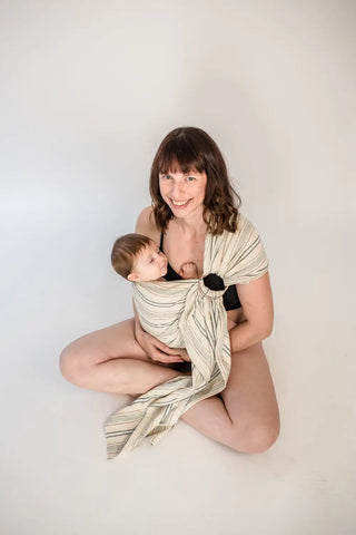 Mother sitting cross legged holding a baby in a ring sling