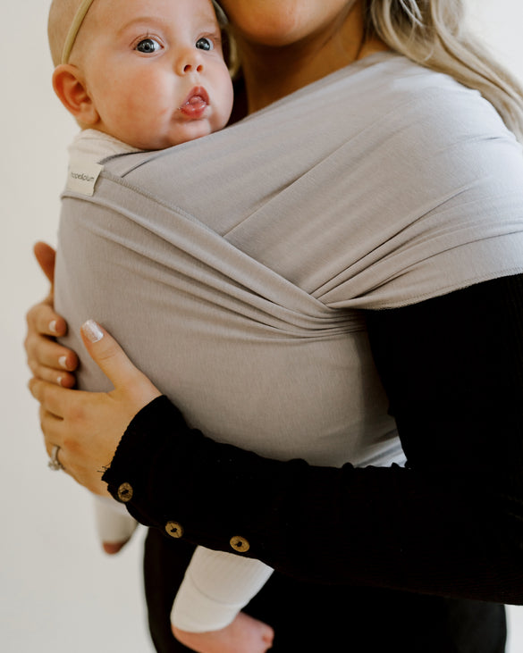 Mother babywearing her baby in a gray baby wrap carrier.