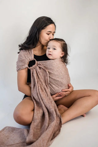 Mother sitting cross legged on the floor wearing her baby in a ring sling.