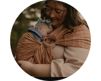 Mother wearing sleeping infant in brown ring sling baby carrier. 