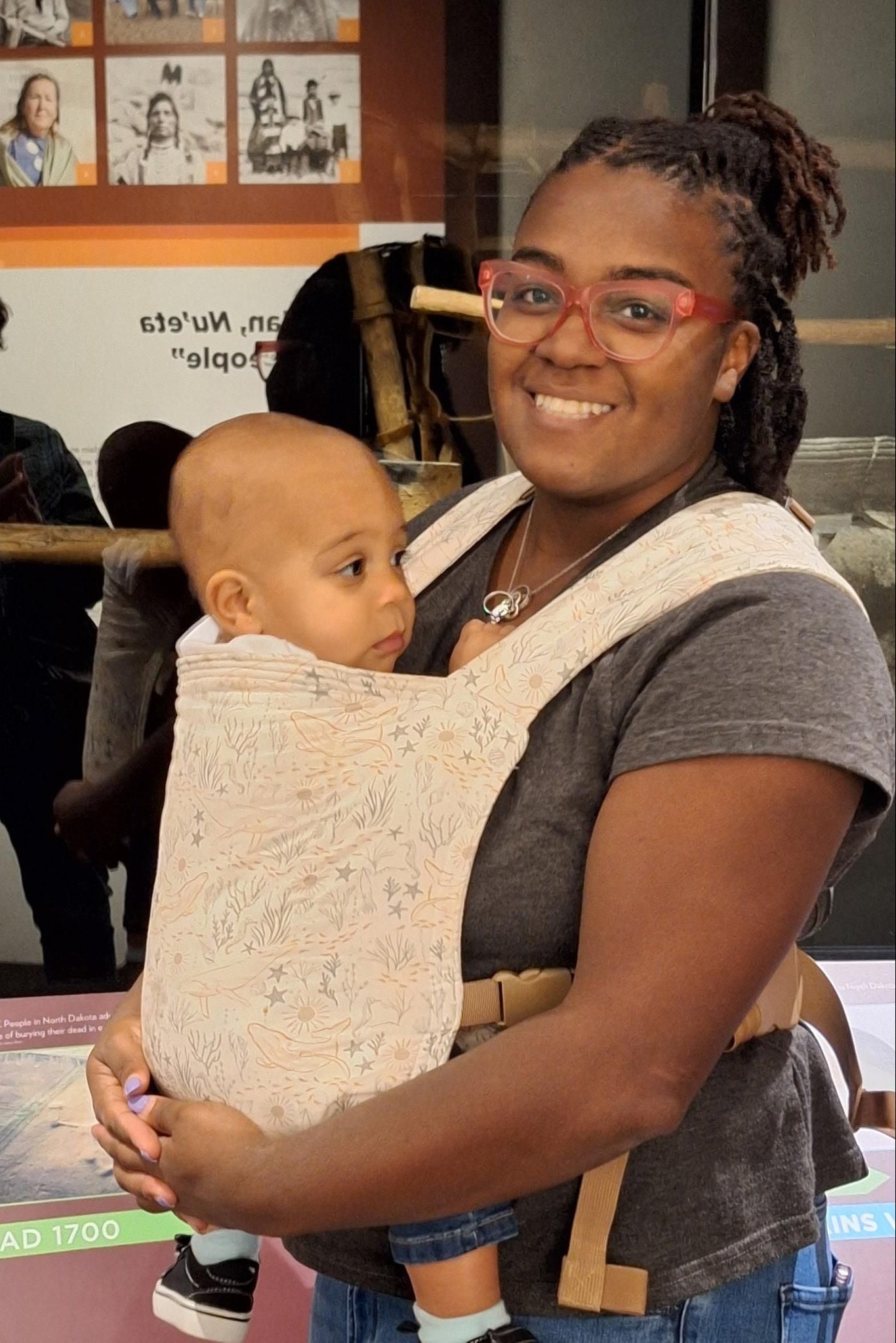 Woman holding a baby in a baby carrier at an exhibit with people in the background