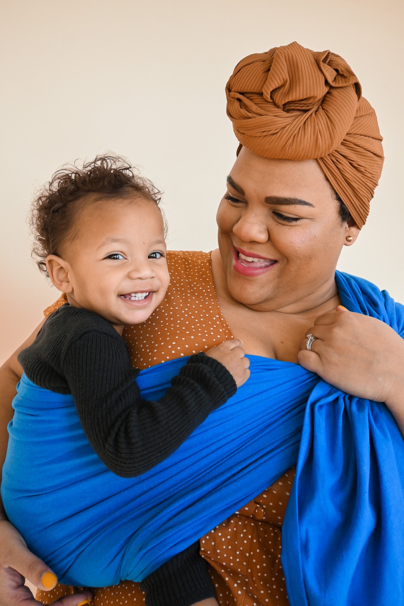 Black mother wearing son in cobalt blue baby wrap sling carrier.