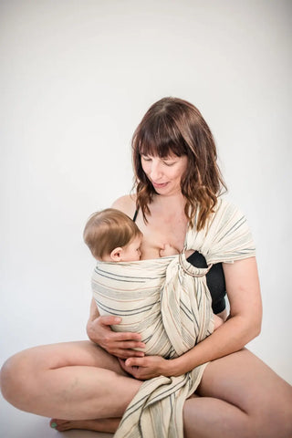 Mother sitting down cross legged holding a baby in a ring sling