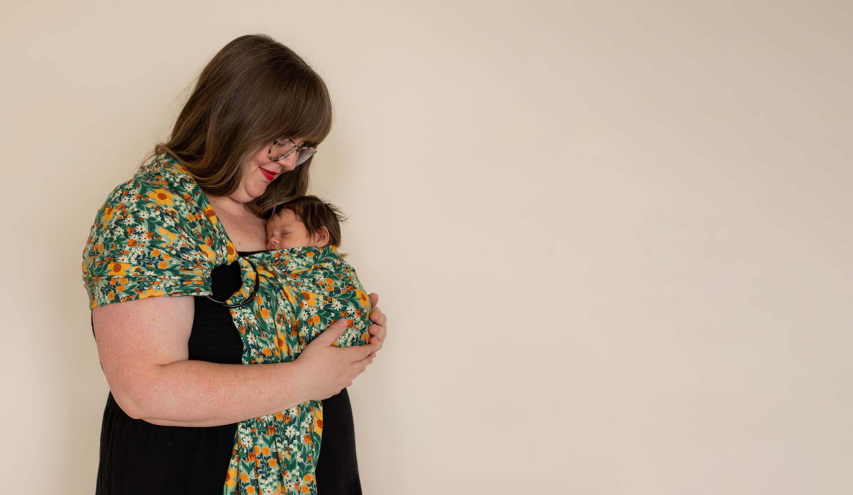 Plus-size mother wearing green floral baby wrap carrier with her newborn baby. 
