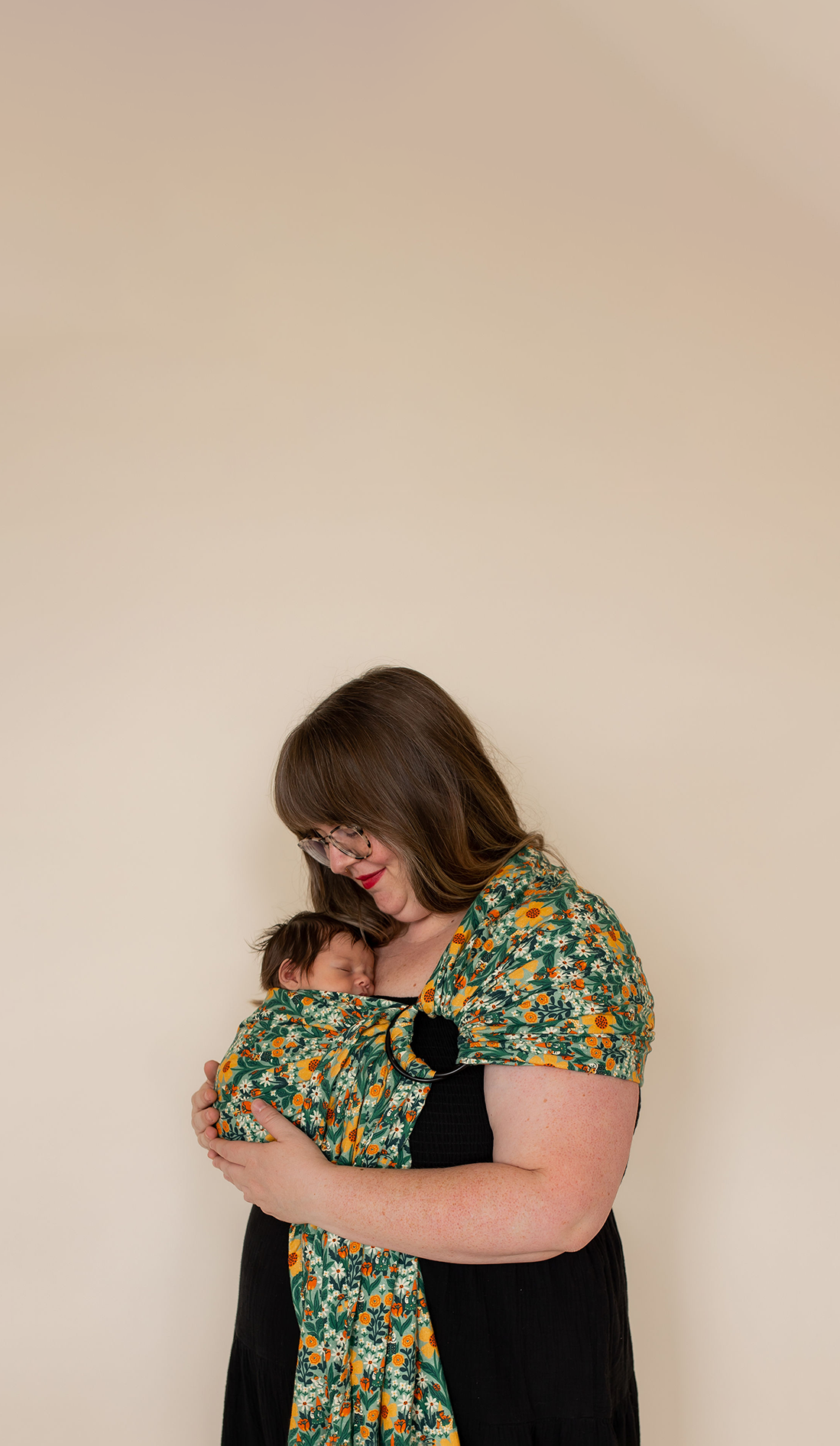 Plus-size mother wearing green floral baby wrap carrier with her newborn baby. 