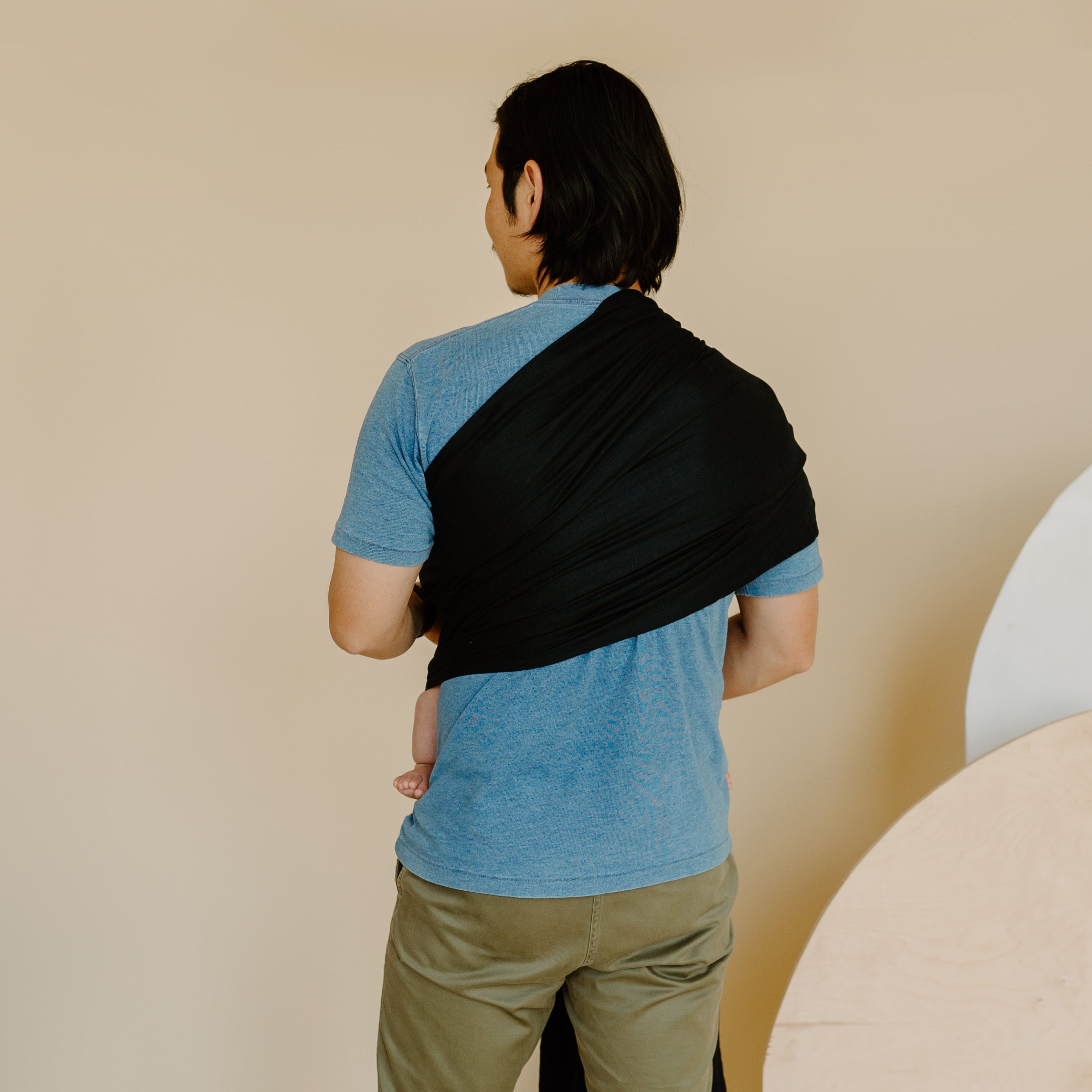 Person wearing a blue shirt and black sling over one shoulder against a beige background