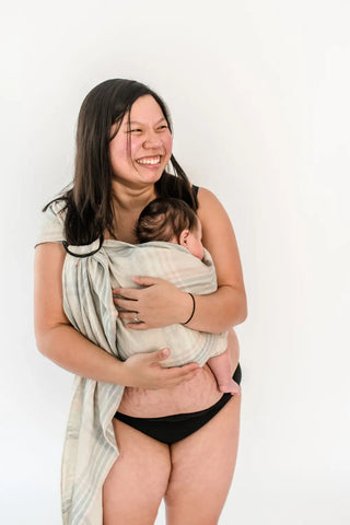 mother in her undergarments holding baby in plaid ring sling