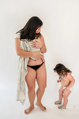 Mother baby wearing an infant in a ring sling. She is looking at her toddler daughter.