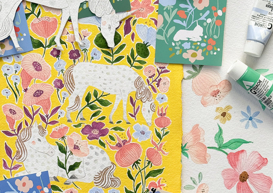 a closeup of an artist's workspace with unicorns and flowers cut out, and gouache paints