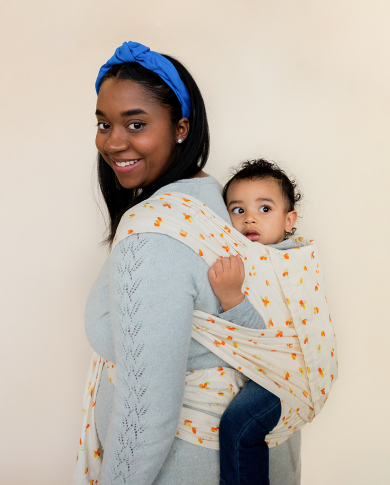 Black mother wearing her baby in a half buckle carrier. 