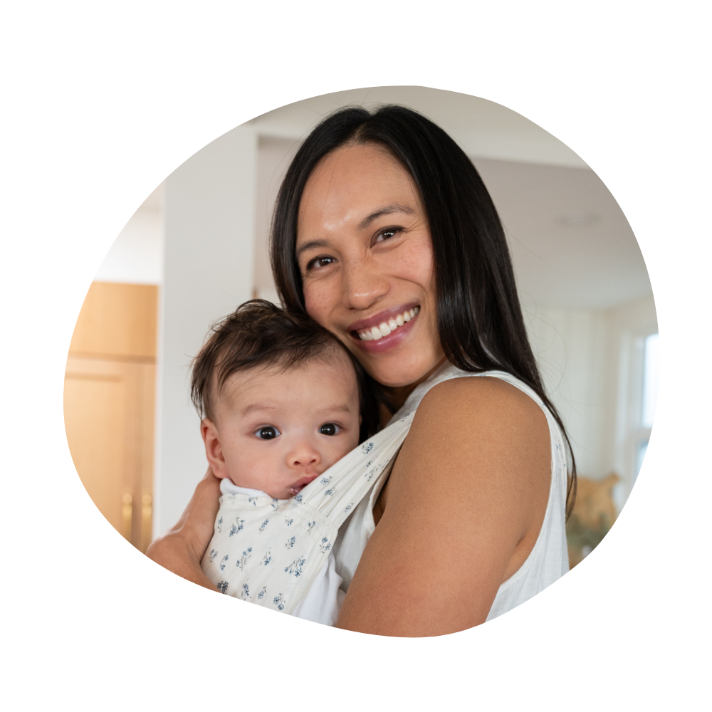 Kelly smiles while holding her son Harvey against her chest in a cream Sprout in Eloise - a blue dainty floral on white.