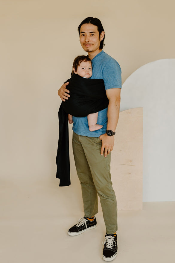 Asian father holding his baby in a black ring sling baby carrier. 