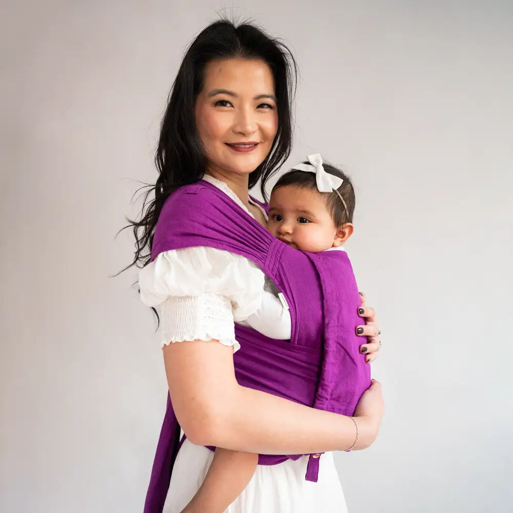 Asian mother in white dress wearing a purple Meh Dai Baby Carrier with her infant