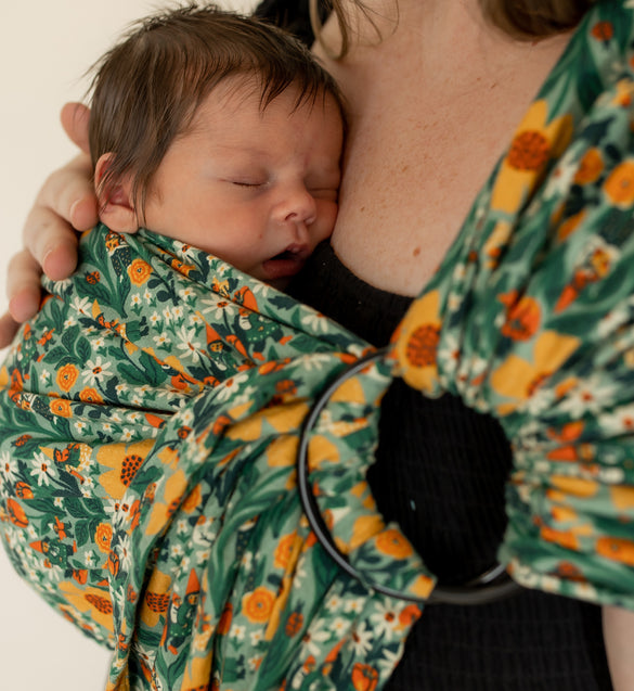Mother wearing green floral print ring sling with a sleeping newborn