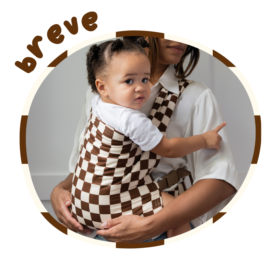 A young toddler is held by a woman in a cute brown and cream checkerboard baby carrier