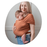 a blonde woman holding her baby in a burnt orange baby wrap