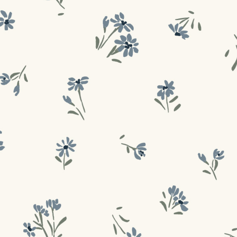 A seamless fabric print of delicate hand-painted florals on a soft cream background. Small dusty blue flowers are scattered in a tossed arrangement, including daisy-like blooms with rounded petals and dark navy centers, plus clusters of smaller buds on slender stems. They're paired with muted sage green leaves and stems in loose watercolor brushstrokes. Tiny green dashes fill the spaces between blooms. The feel is light, airy, and botanical, with a vintage cottage or prairie sensibility.