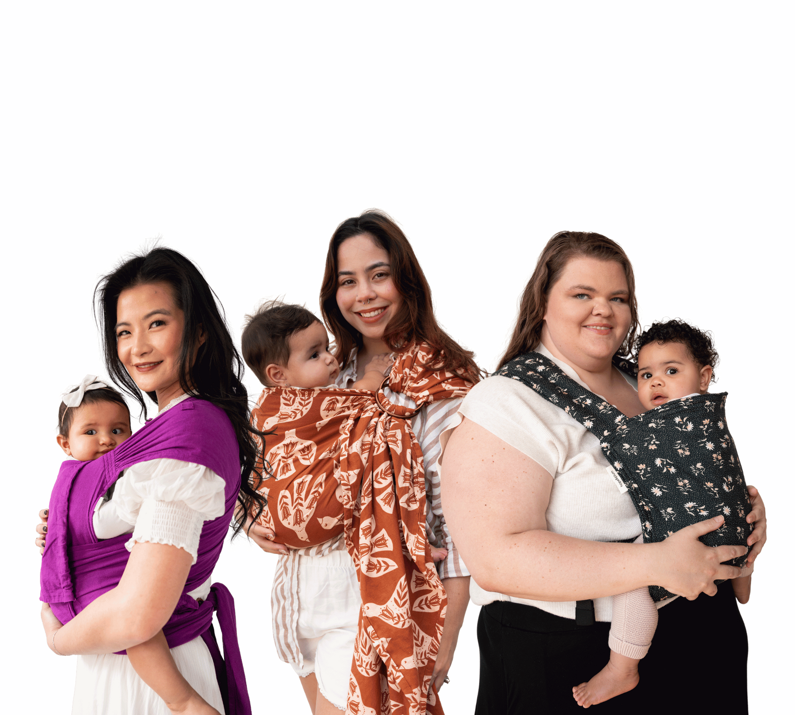 Three caregivers each carry a baby on a transparent background — left: Aster meh dai in solid purple; centre: Wren ring sling in rust with cream folk-art birds; right: Daisy Lark in dark charcoal with small white floral sprigs.