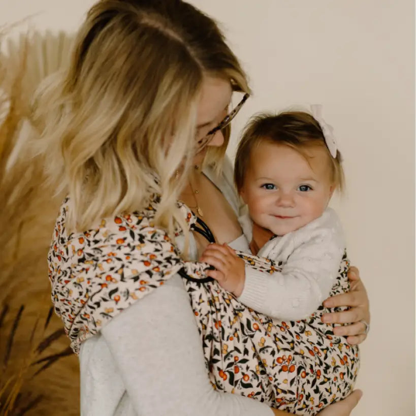 blonde white woman holding blonde baby in citrus patterned ring sling