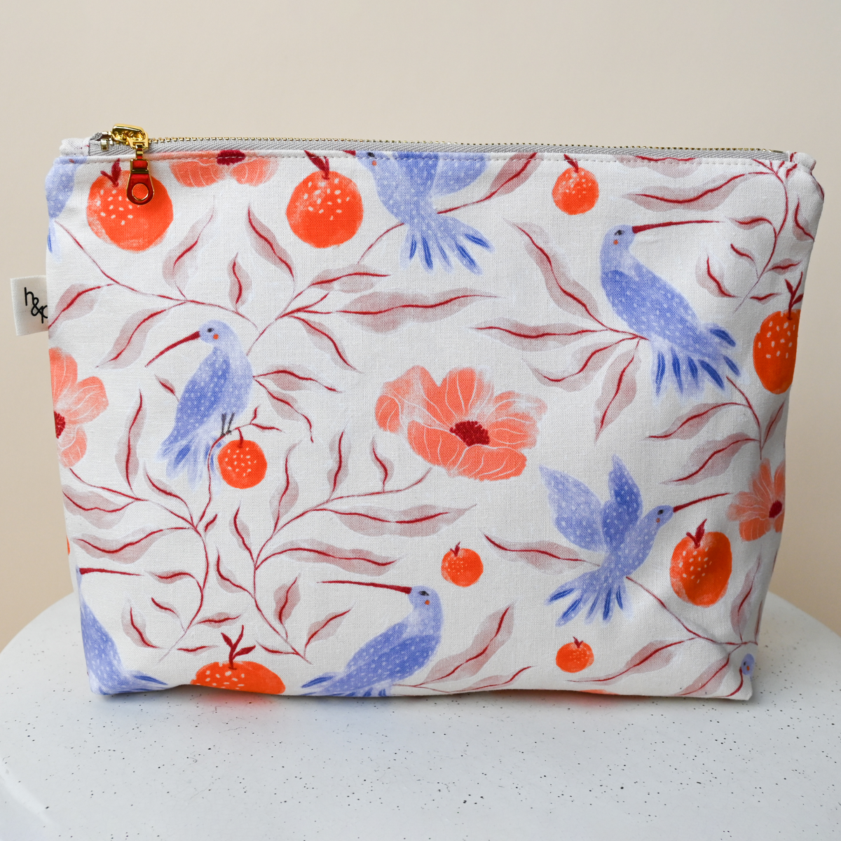 Large Flat Bottom Bag in Ambrosia, a standing zip pouch with a gold zip, cream fabric hand-painted with blue hummingbirds, orange pomegranates and coral poppies.