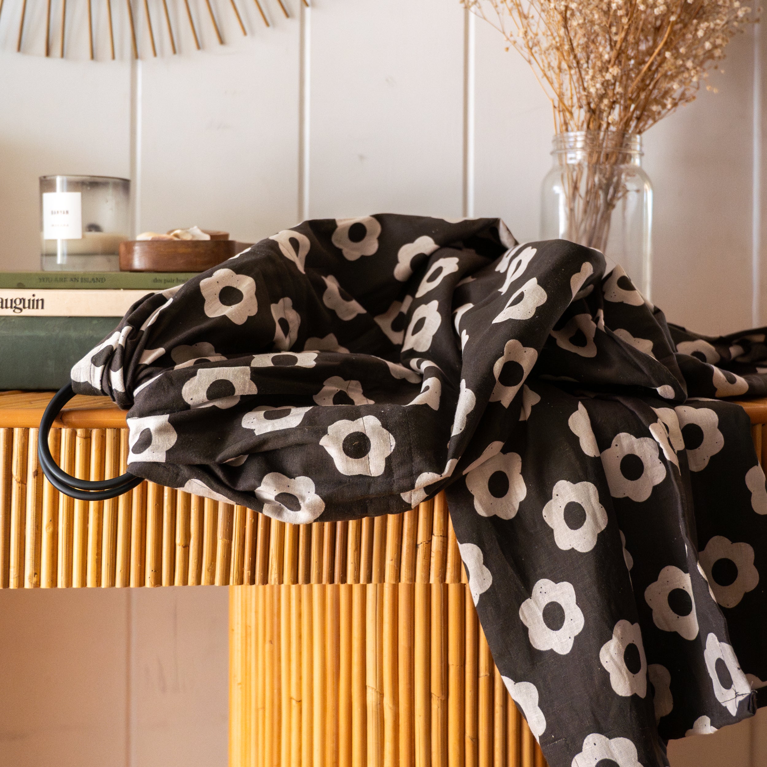 Black ring sling with white floral pattern draped over a wooden surface with a neutral background