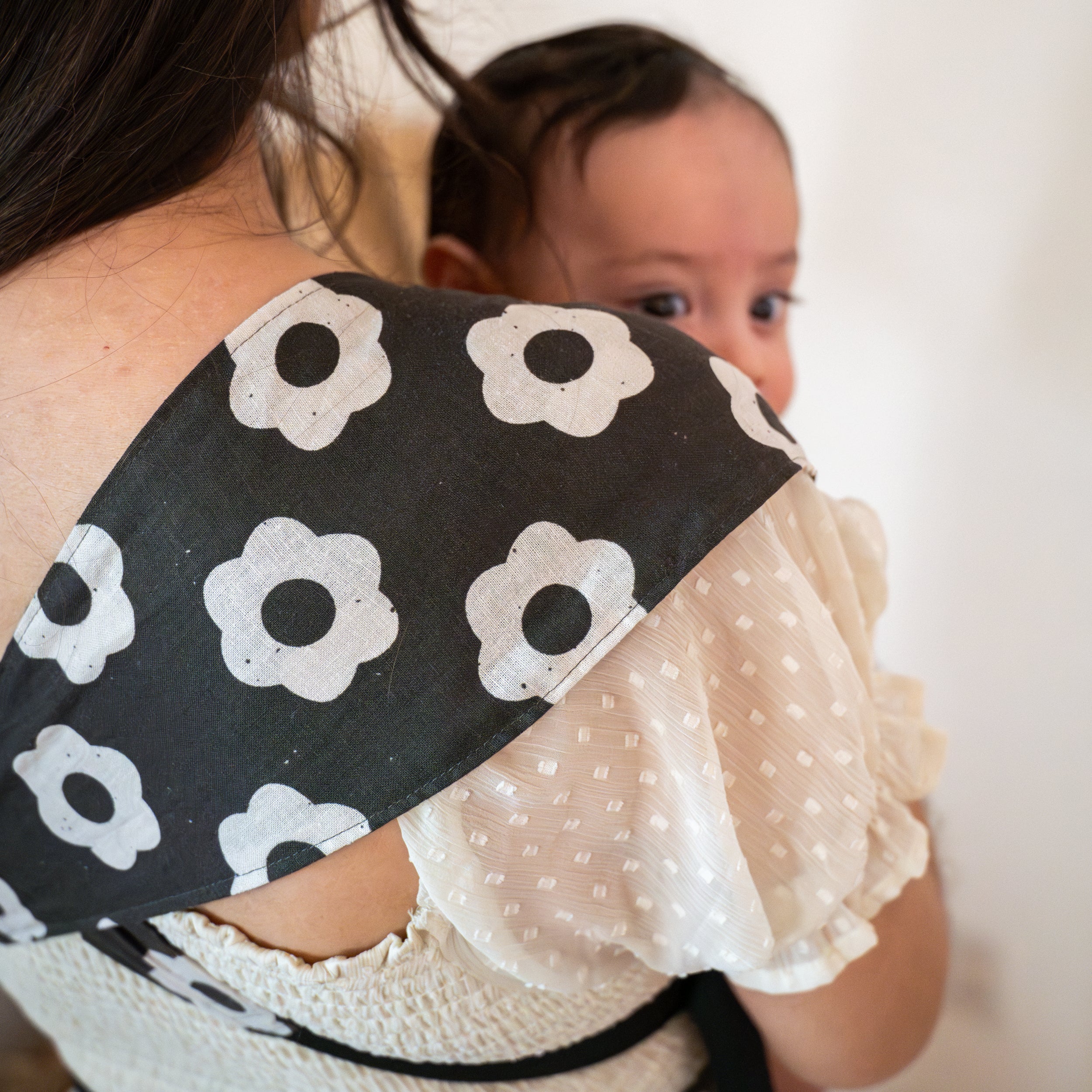 Person wearing a black and white floral-patterned baby carrier with a baby peeking out.