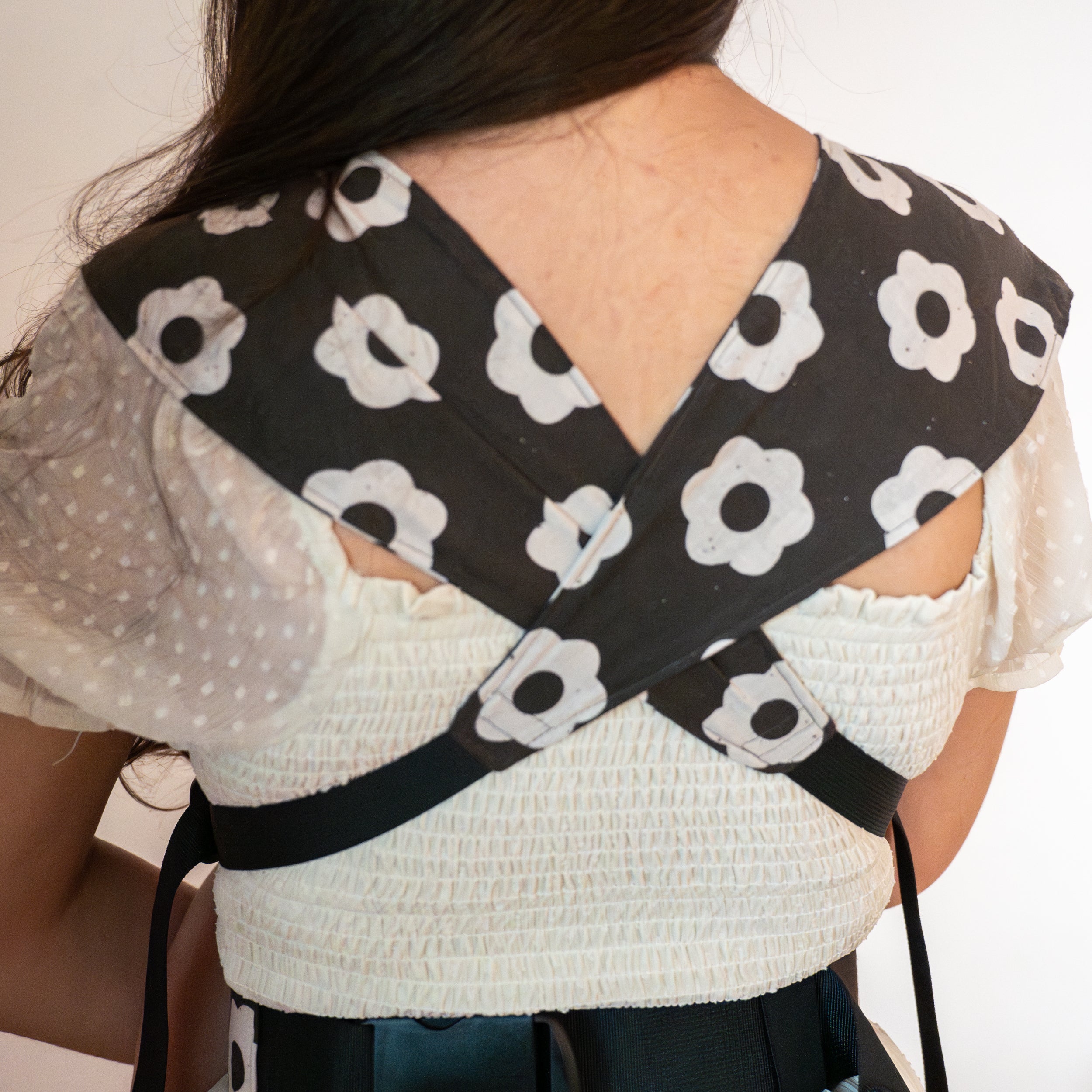 Person wearing a black and white floral-patterned newborn buckle baby carrier.