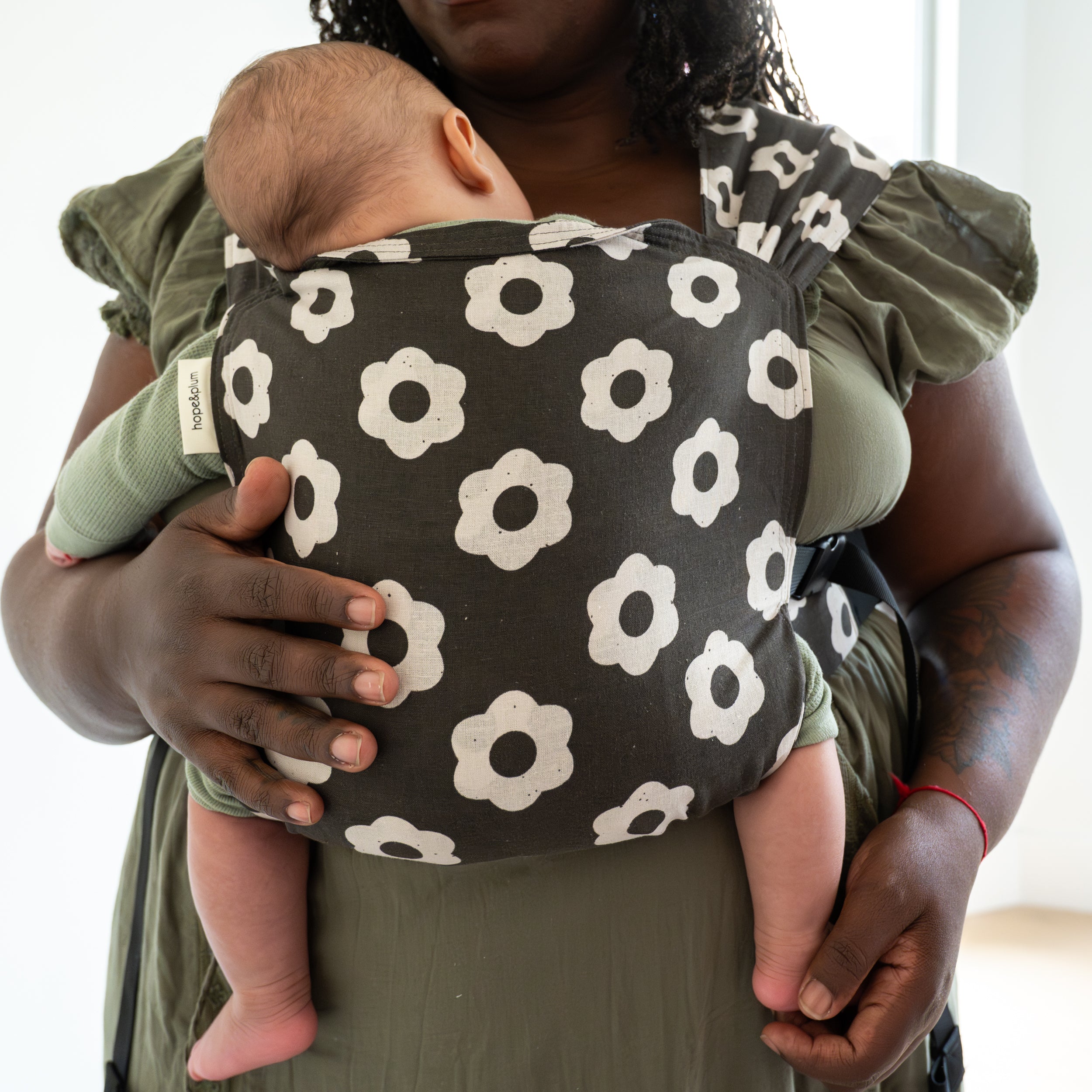Person holding a baby in a black and white floral-patterned newborn carrier with a neutral background