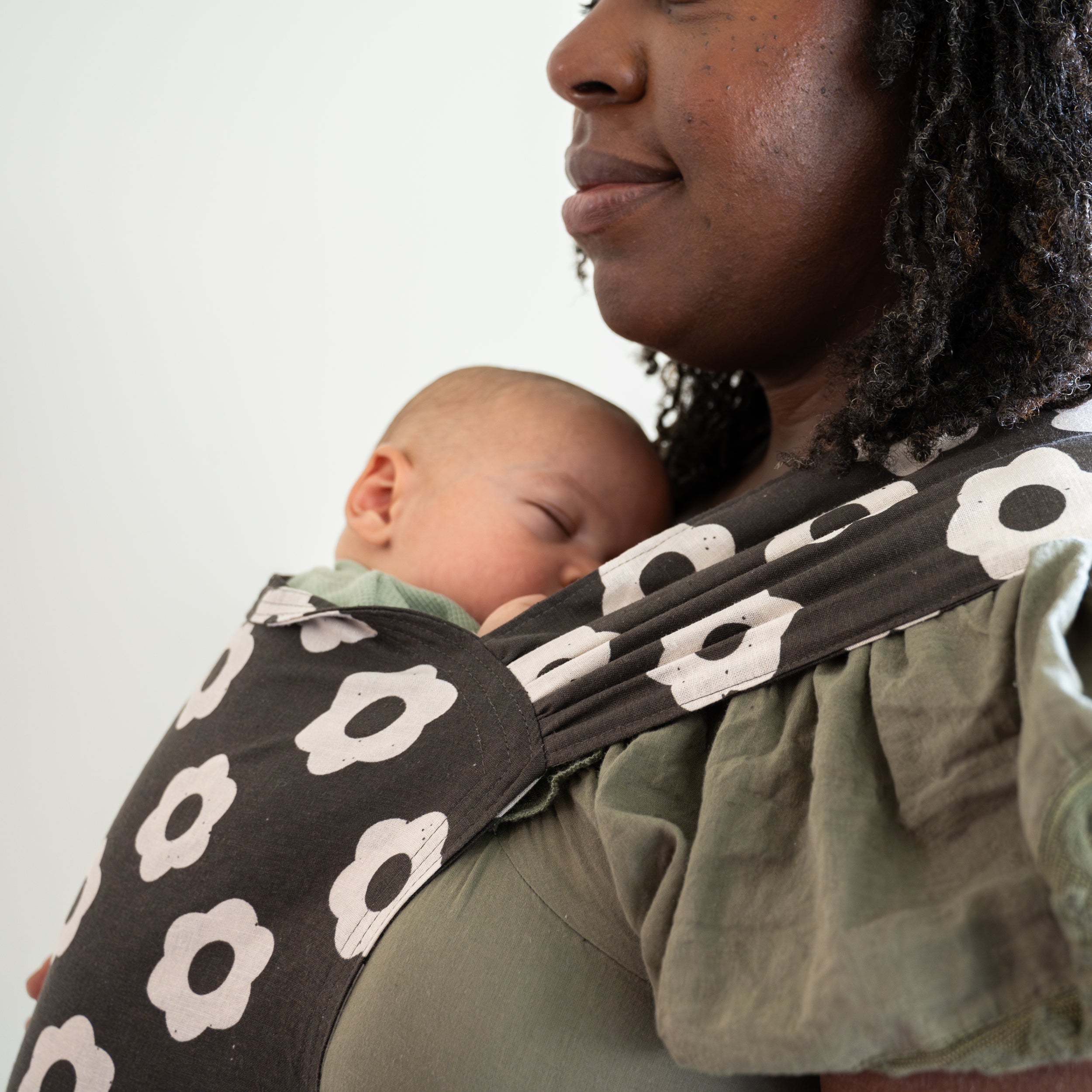 Person wearing a black and white floral-patterned newborn buckle baby carrier.