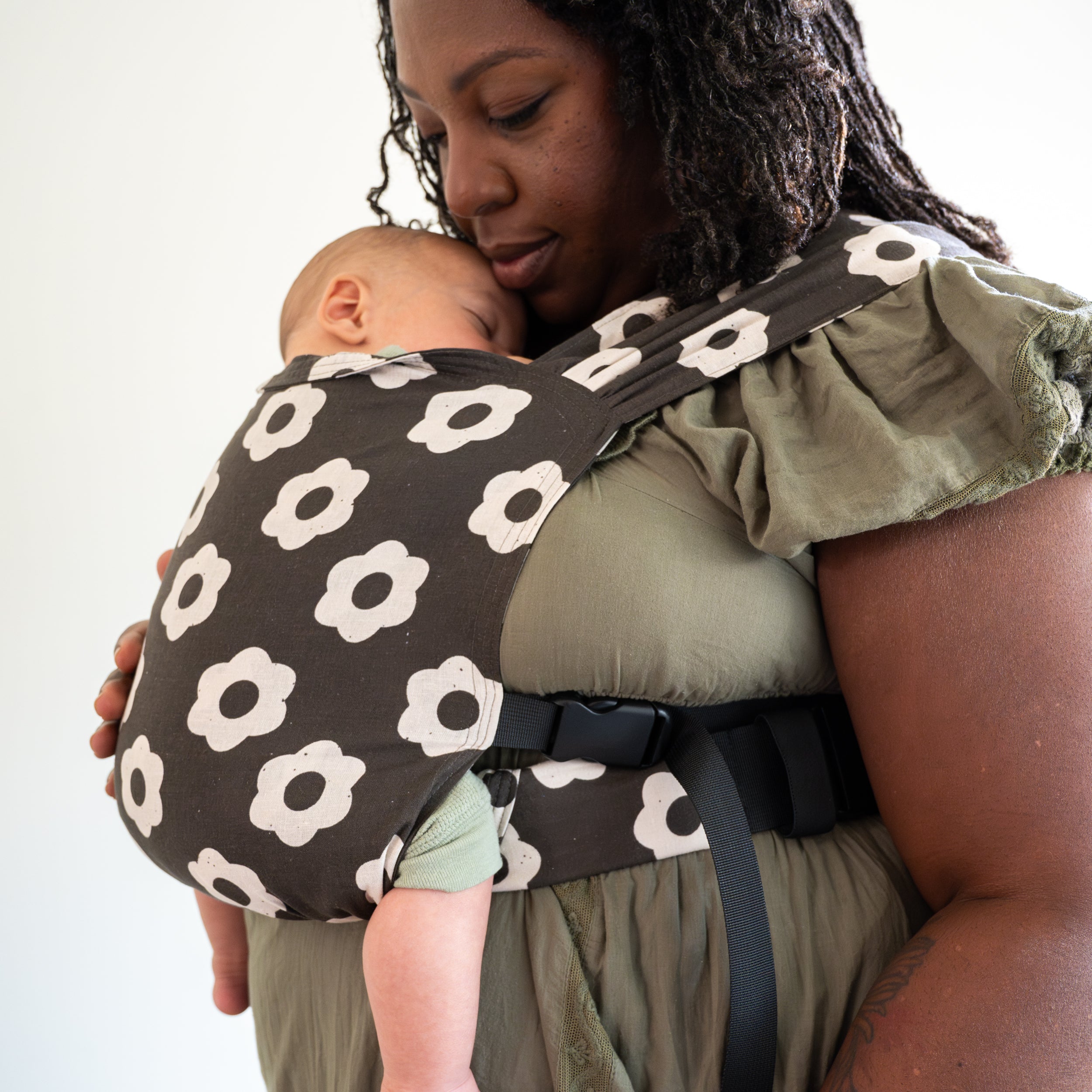 Woman holding a baby in a floral-patterned carrier against a white background