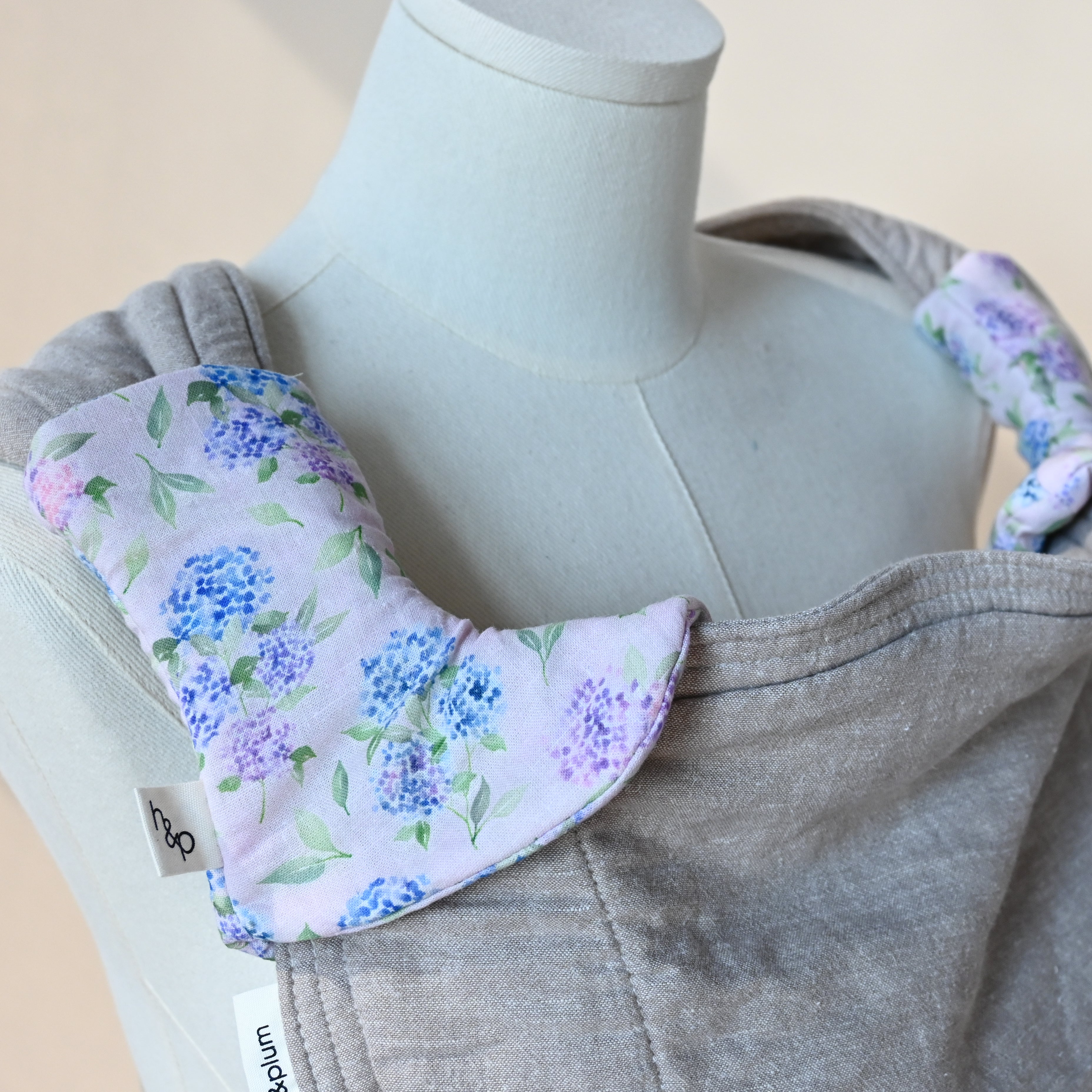 Drool Pads in Blush — strap covers wrapped around a carrier's shoulder straps, blue and lavender hydrangea print on a soft pink background.