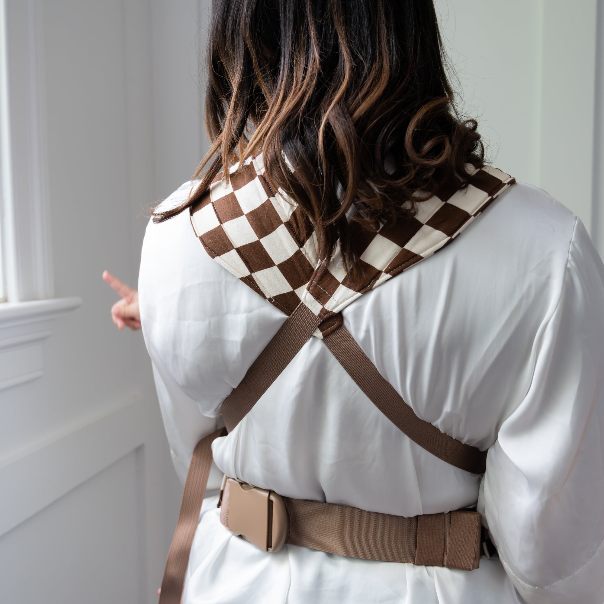 Woman holding a child in a brown and white checkered baby carrier against a neutral background