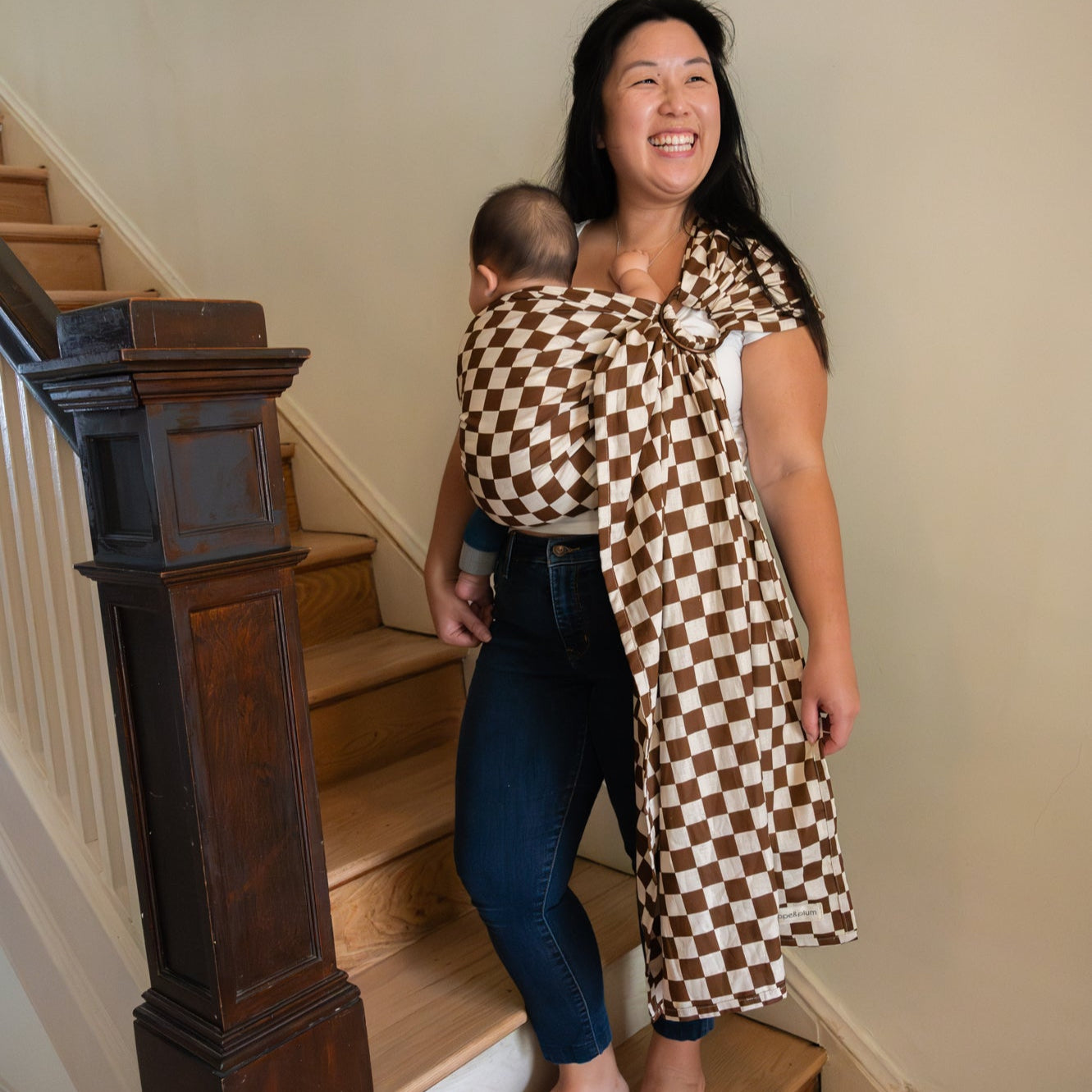 Woman carrying a baby in a checkered wrap sling on a staircase
