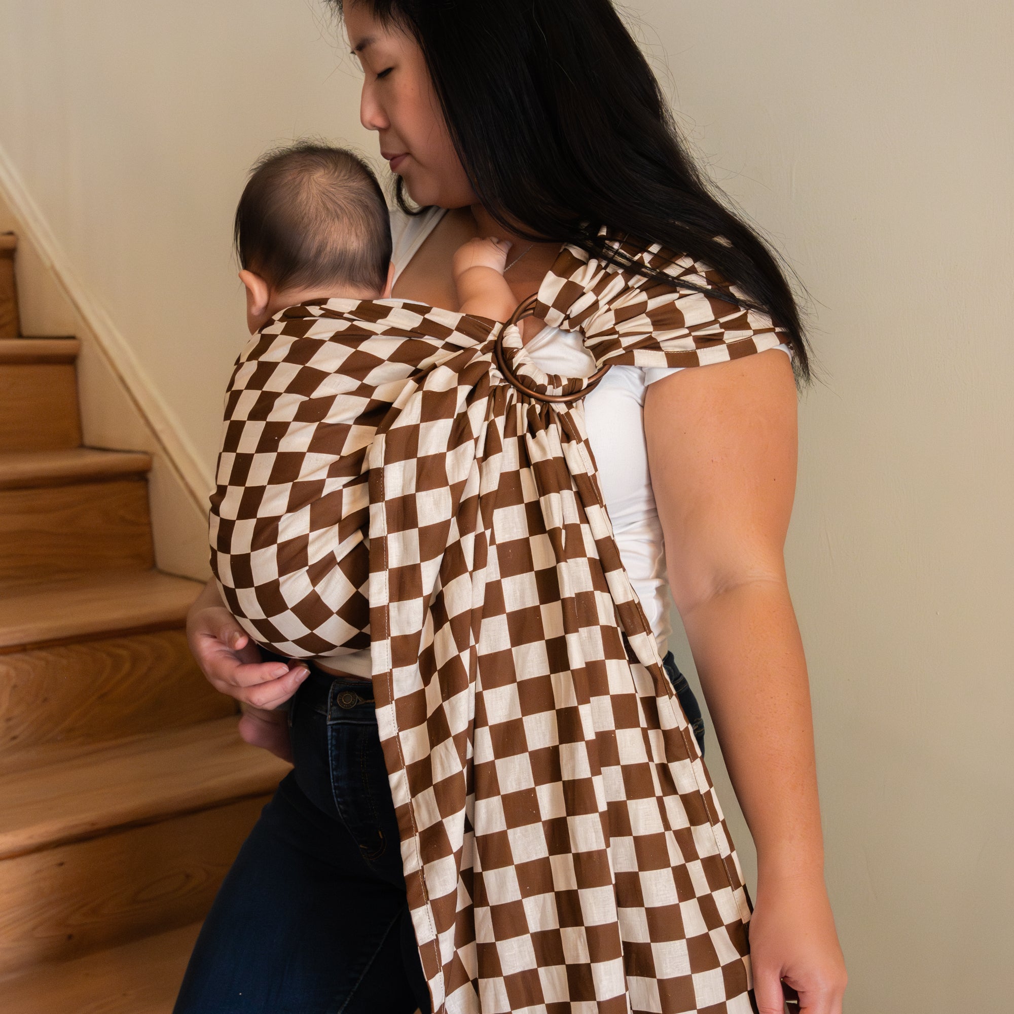 Woman carrying a baby in a brown and white checkered sling at home.