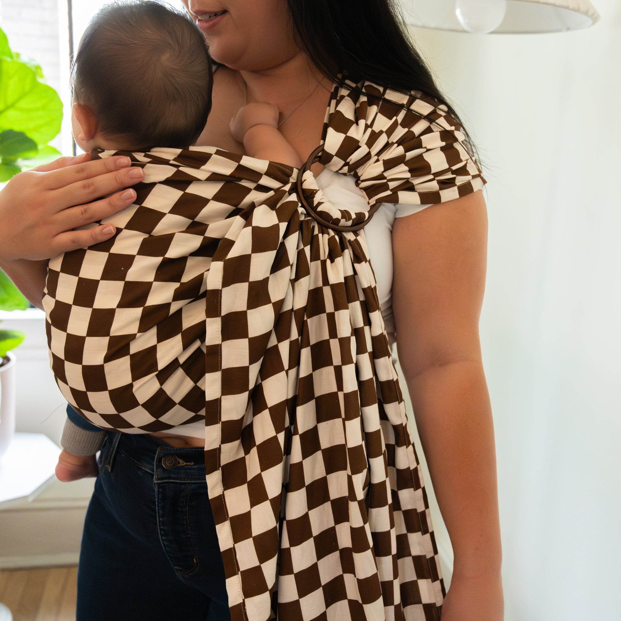 Person holding a baby wrapped in a brown and white checkered wrap against a white background
