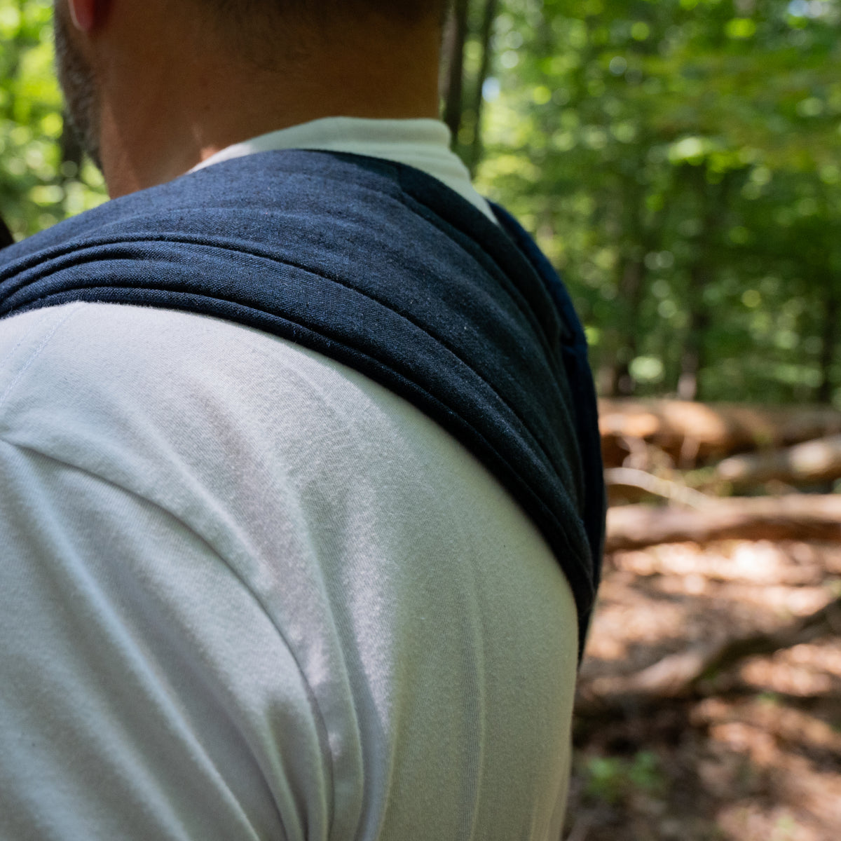 Close view of the Caspian carrier strap over the wearer's shoulder in woodland, showing the deep indigo woven chambray.