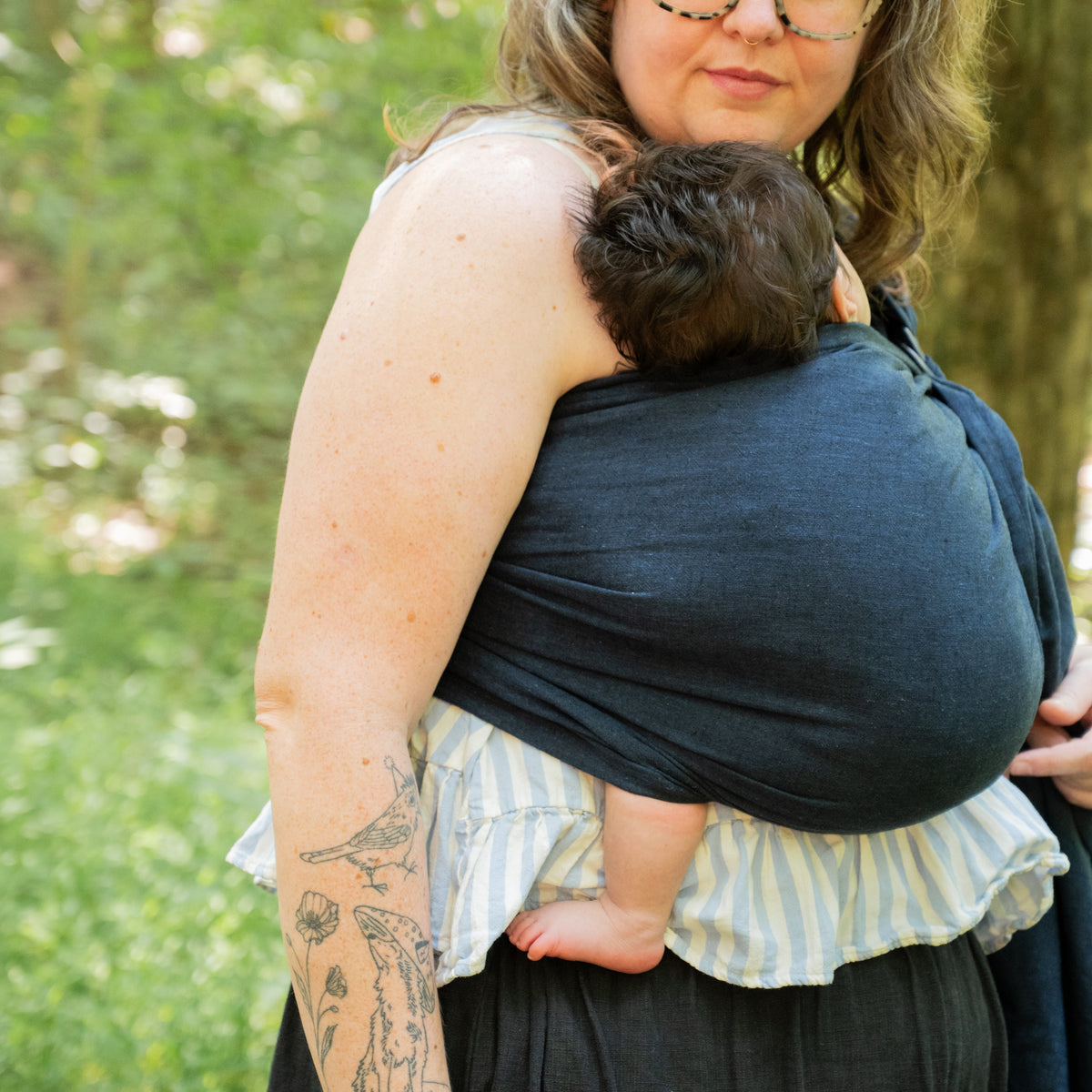 Side view of a baby sleeping in the Caspian Ring Sling, the indigo chambray pouch supporting them against the wearer's chest.