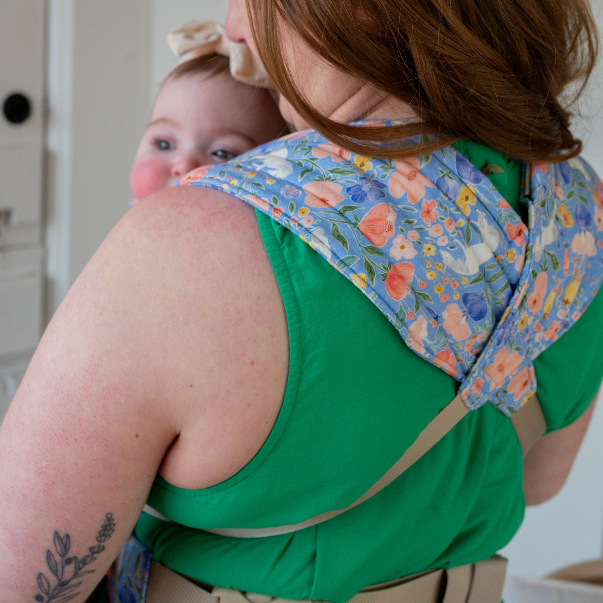 Woman carrying a baby in a floral unicorn patterned carrier.