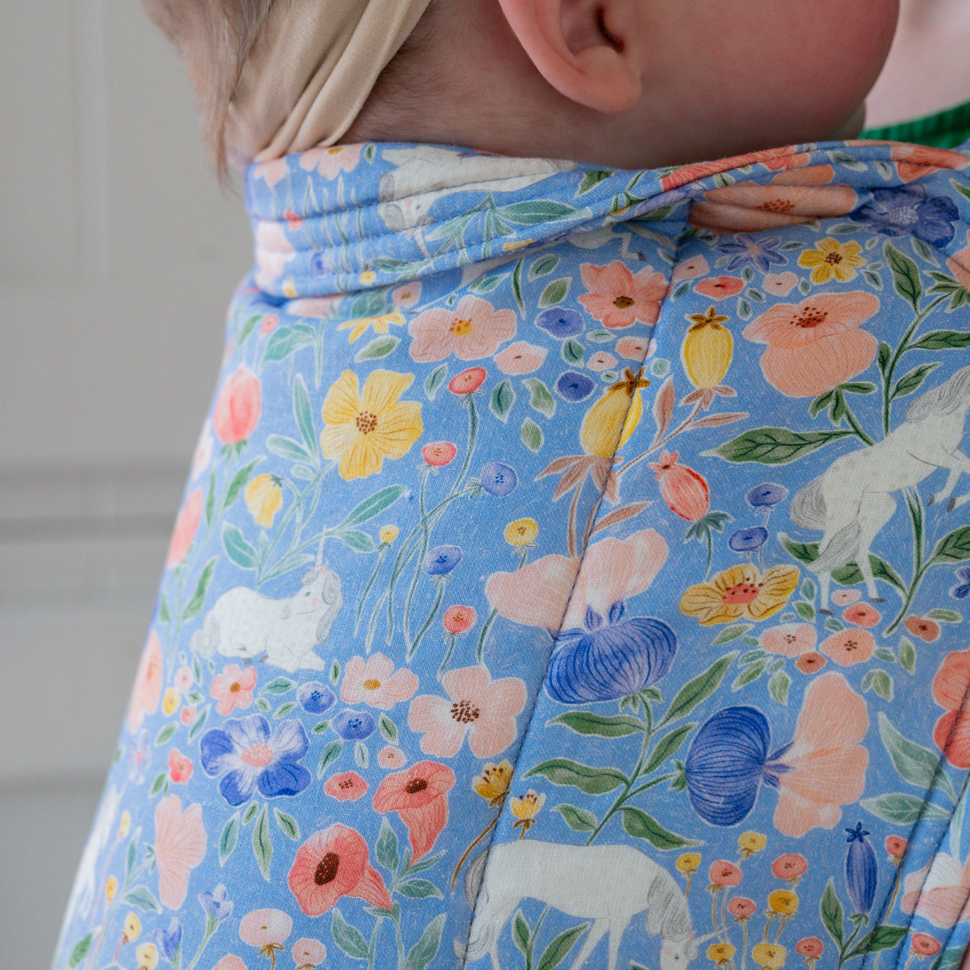 Woman carrying a baby in a floral unicorn patterned carrier.
